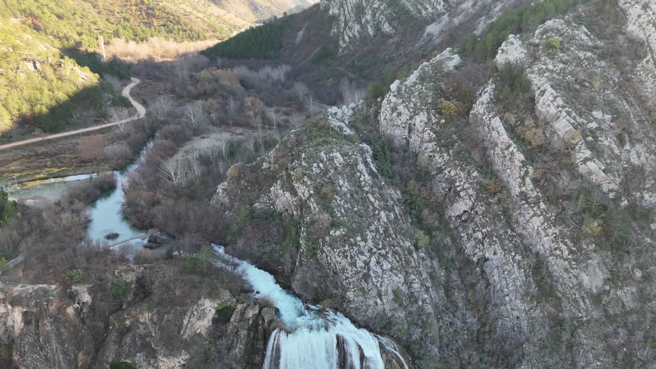 Static drone shot with camera movement following the upper flow across Krčić Waterfall, revealing the river below. Shaded gorge, mighty waterfall, and the Krka River near Knin, Croatia