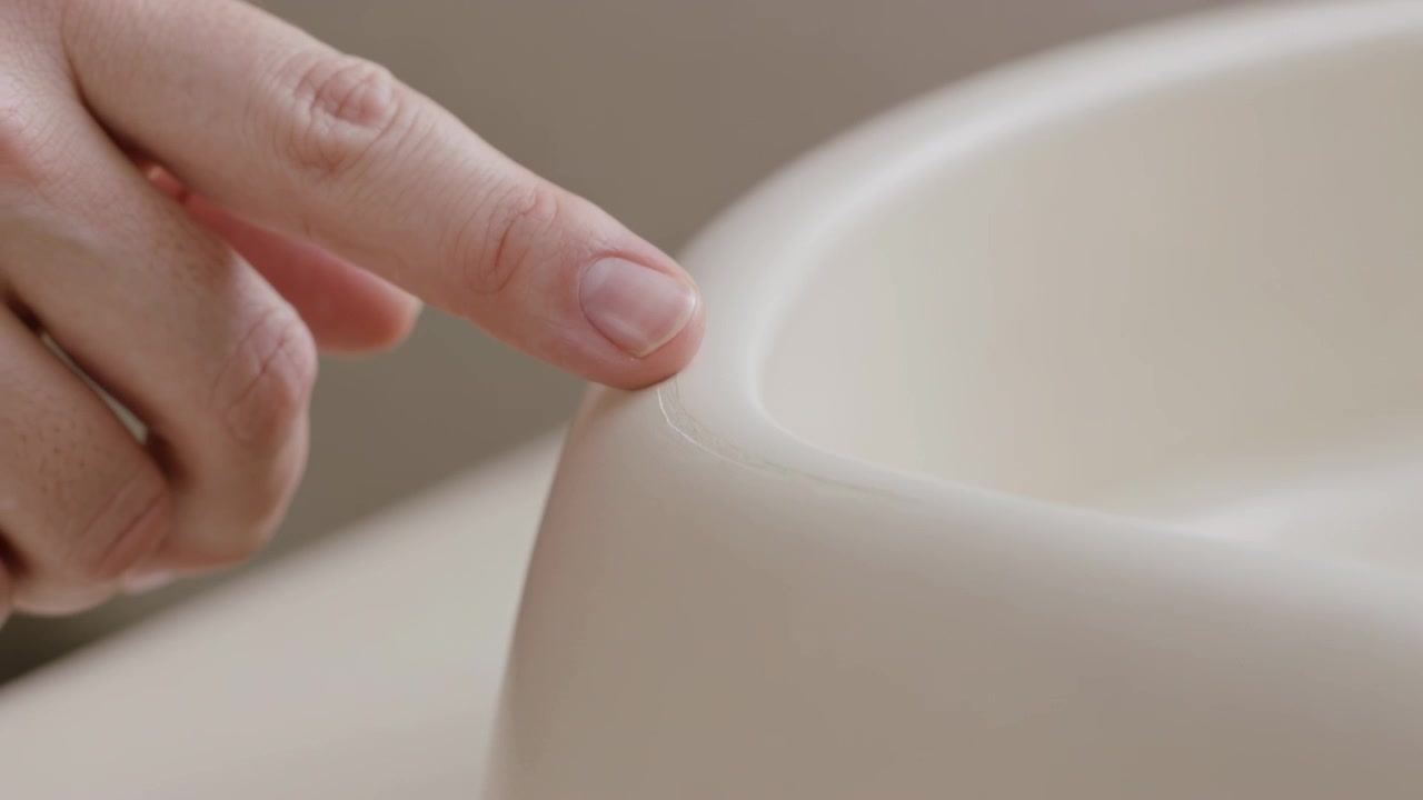 Moving left hand into frame fingertip tracing cream rim at tabletop feeling contour with metal ring