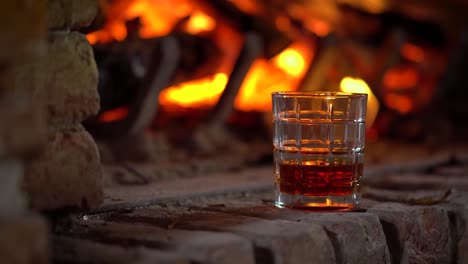 glass with a drink on a chimneypiece with a fire burning in the background, static shot