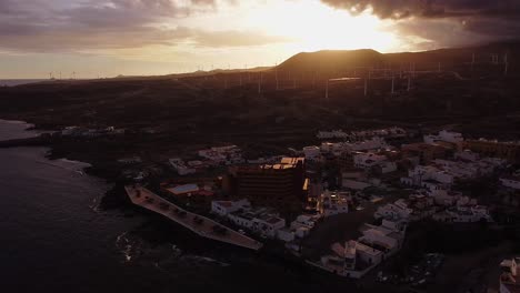 picturesque aerial, town with houses and windmills at coast beach of island tenerife during golden hour evening summer sun, panning shot