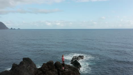 Adventurous-woman-stands-on-rugged-cliffs-at-madeira-coast-during-bright-sunrise