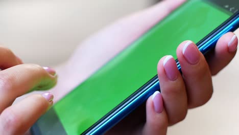 a woman is sitting in a cafe with a smartphone in her hands with a green screen mockup. the girl browses the internet, watches content, videos, blogs.