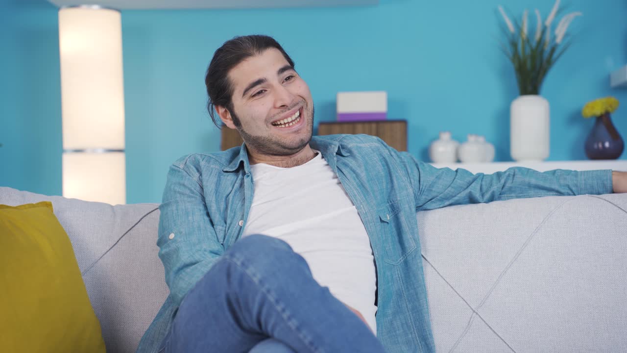 유쾌하고 유쾌한 젊은이가 소파에 앉아 있습니다.
