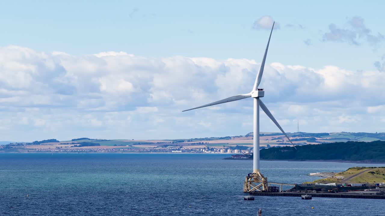 Large offshore wind turbine spins steadily in daylight, coastal landscape, wide static shot, Dundee