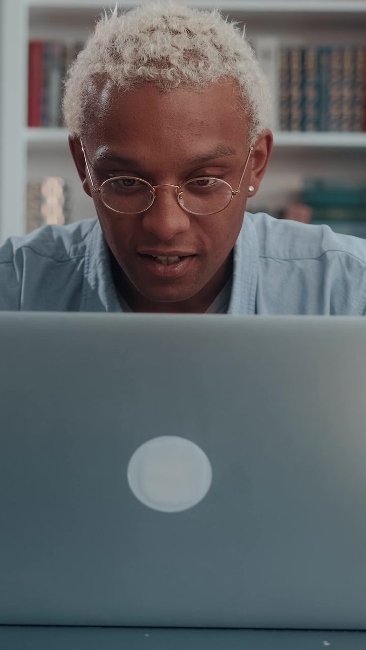 Konzentrierter junger afroamerikanischer Mann, der sich tief auf seinen Laptop konzentriert und ihn dann öffnet