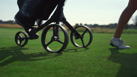 golfer carry sport equipment trolley clubs bag. golf player legs walk on course.