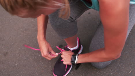 una rubia en forma atando el cordón de sus zapatos.
