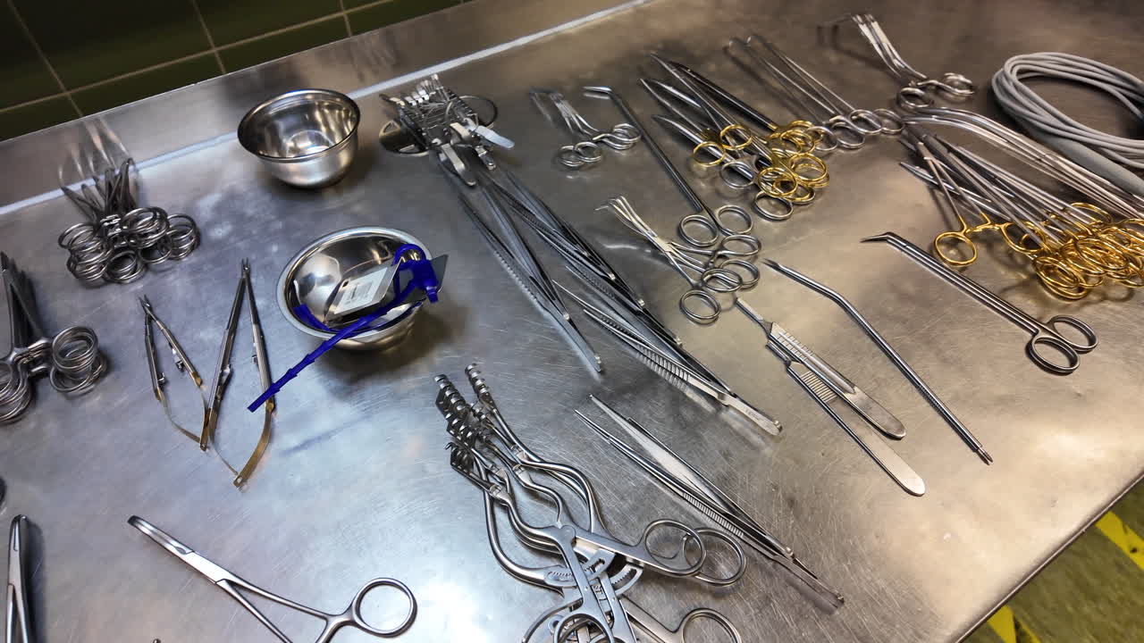 Vista aproximada de instrumentos cirúrgicos estéreis cuidadosamente organizados sobre uma mesa de aço inoxidável em uma sala de cirurgia hospitalar. A imagem mostra pinças, tesouras, grampos e porta-agulhas.