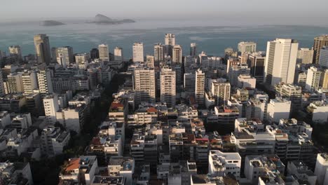 aerial closing in showing ipanema neighbourhood in rio de janeiro with high rise and low rise buildings revealing islands just outside the coast at sunrise