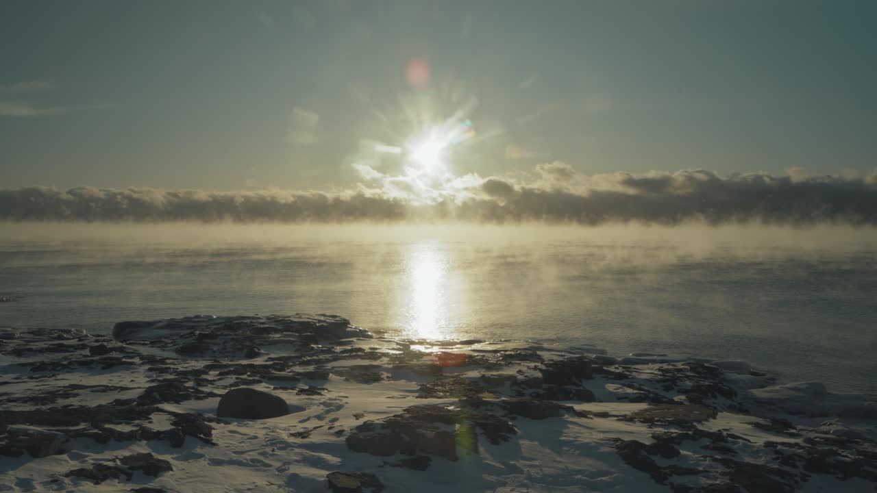 Breathtaking sunrise over a frozen Lake Superior, with the sun's lens flare reflecting off the ice and rising sea smoke