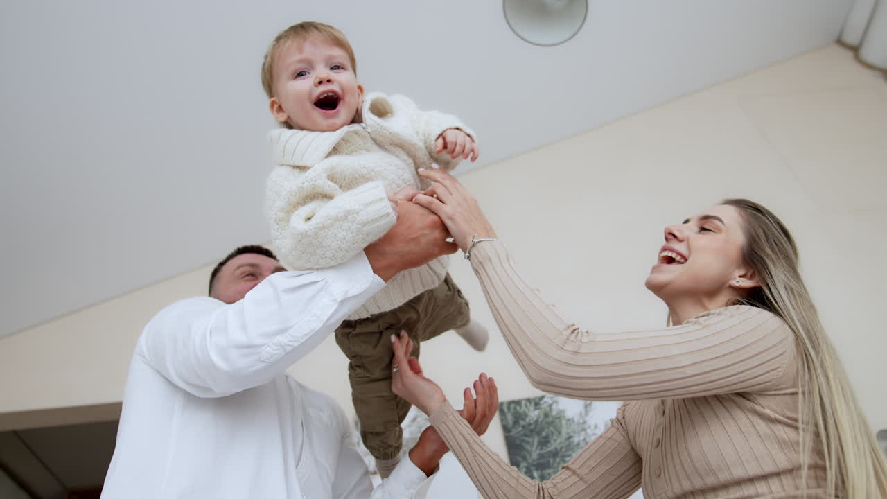 Loving mom and dad hold their lovely son waving him up and down. Parents play with their beloved baby.