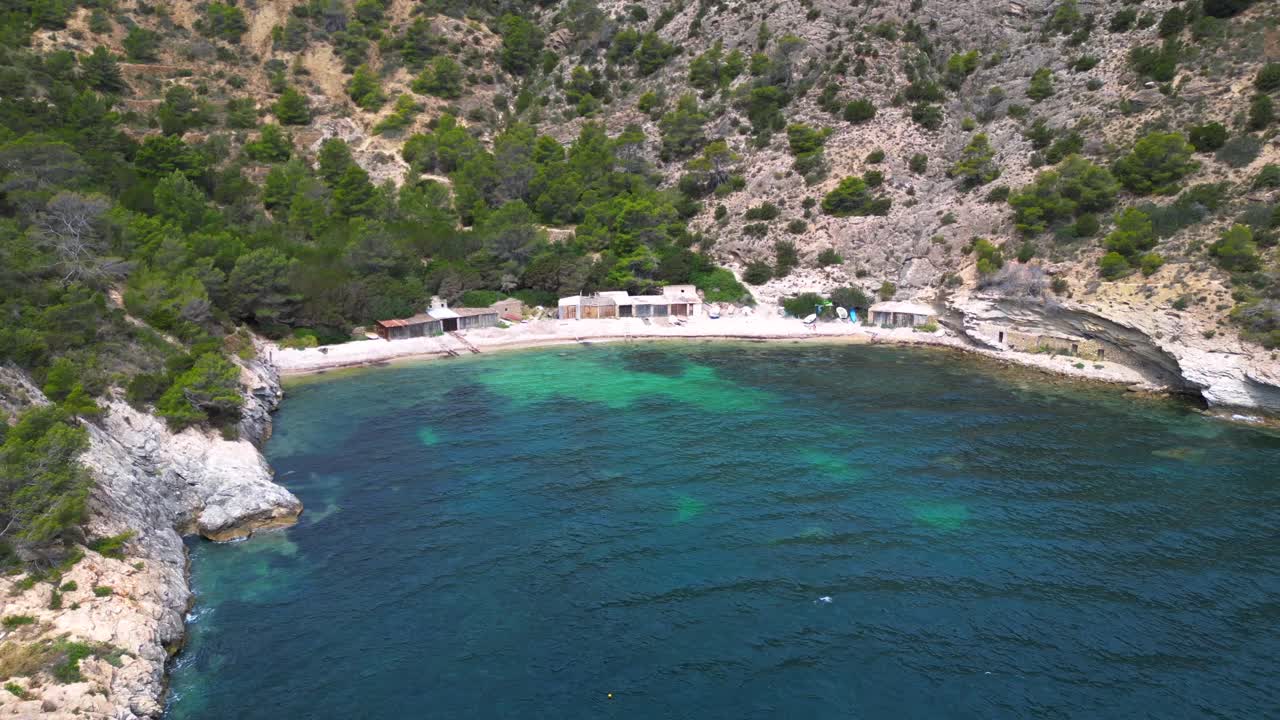 Cala Llentrisca beach with turquoise water and Barques de pescadors Huts in Ibiza, Spain, in summer. Lovely aerial view flight drone shot from above