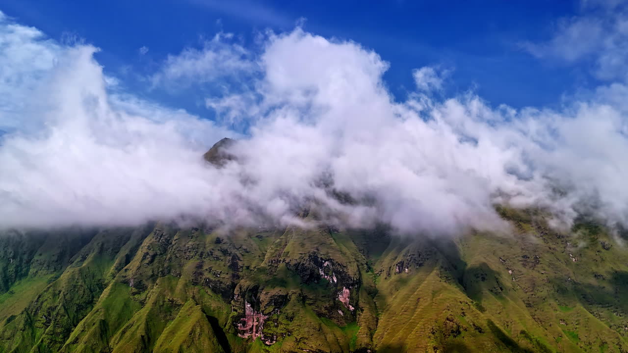 Aerial view of Bukit Selong in Sembalun, Lombok, showing dramatic green hills and misty clouds beneath a vivid blue sky near Mount Rinjani