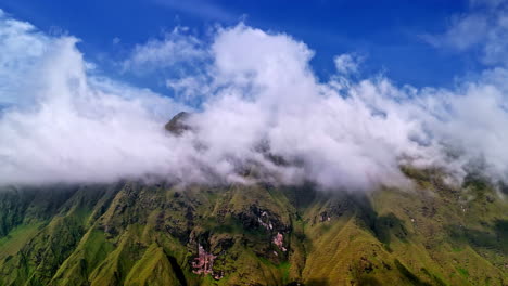aerial view of bukit selong in sembalun, lombok, showing dramatic green hills and misty clouds beneath a vivid blue sky near mount rinjani