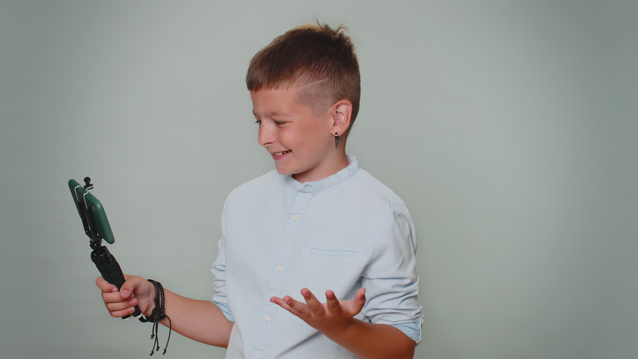 블로거 소년은 휴대 전화로 셀피를 찍고 셀피 스틱을 붙여 가입자와 온라인으로 비디오 통화를 합니다.