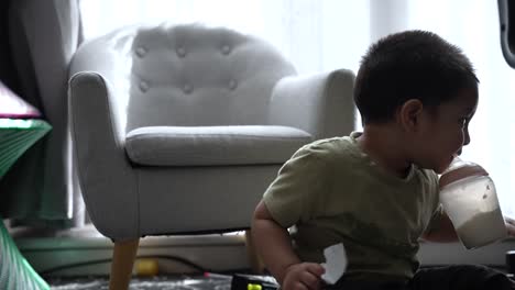 south asian 18-month-old toddler boy drinking milk while sitting on the floor at home and being playful