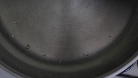 slow-motion perspective of water droplets merging into a larger drop, showcasing the non-stick feature of a stainless pan