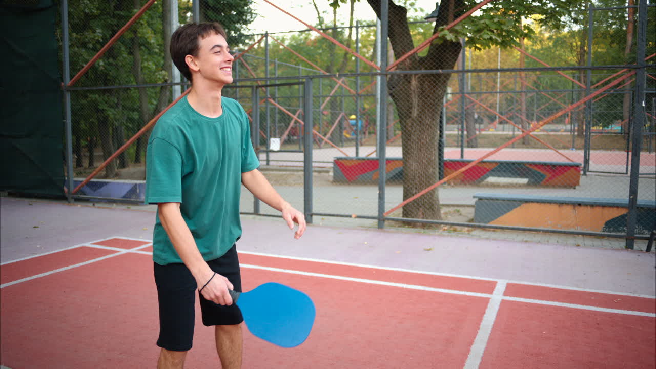 Boys playing pickleball with yellow ball and blue paddle at a court