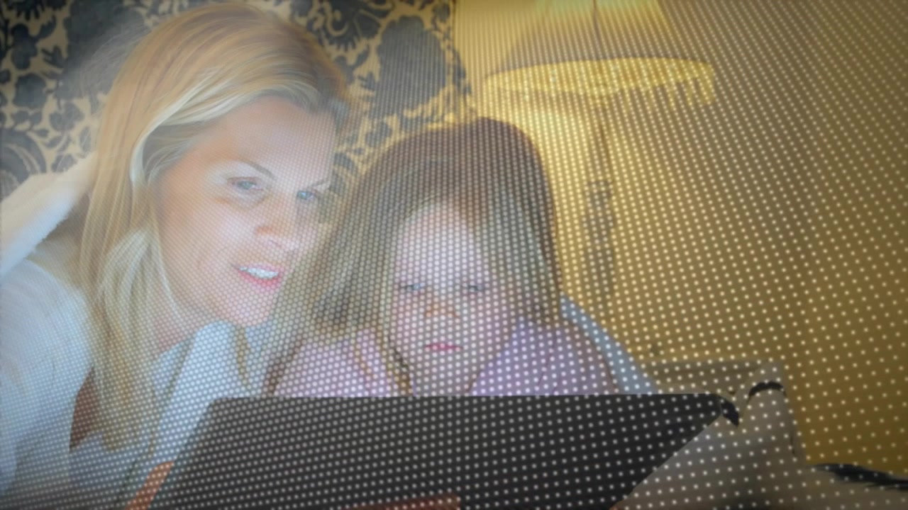 Matka se naklání a ukazuje na tablet v posteli, s tečkovaným filtrem a pomáhá dítěti s učením.