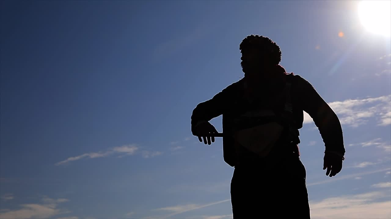 Backlit camera footage of a man playing zeybek on the hill with his local clothes