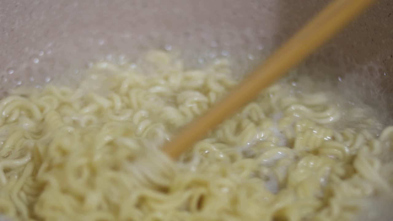 箸でかき混ぜながら麺を茹でるクローズアップ