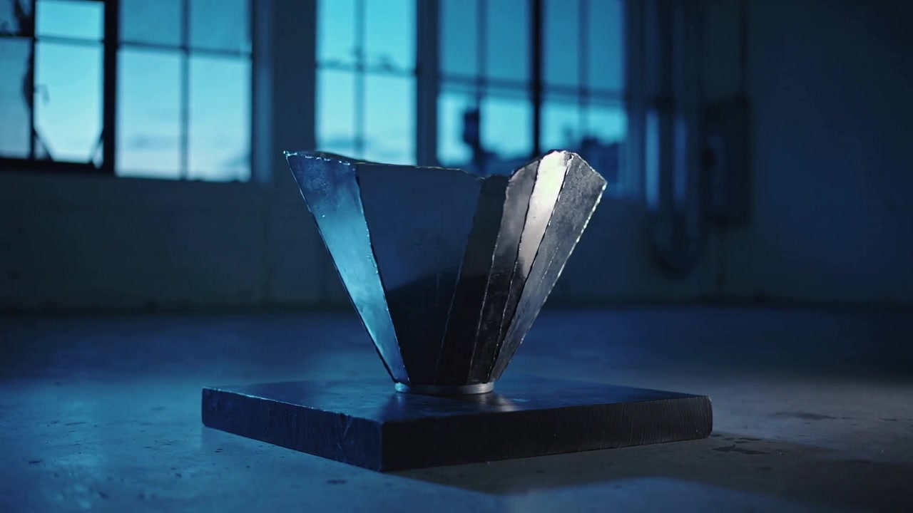 Meccanismo che attiva l'apertura di pannelli di scultura metallica che ruotano su una base in un loft, rivelando la forma interna
