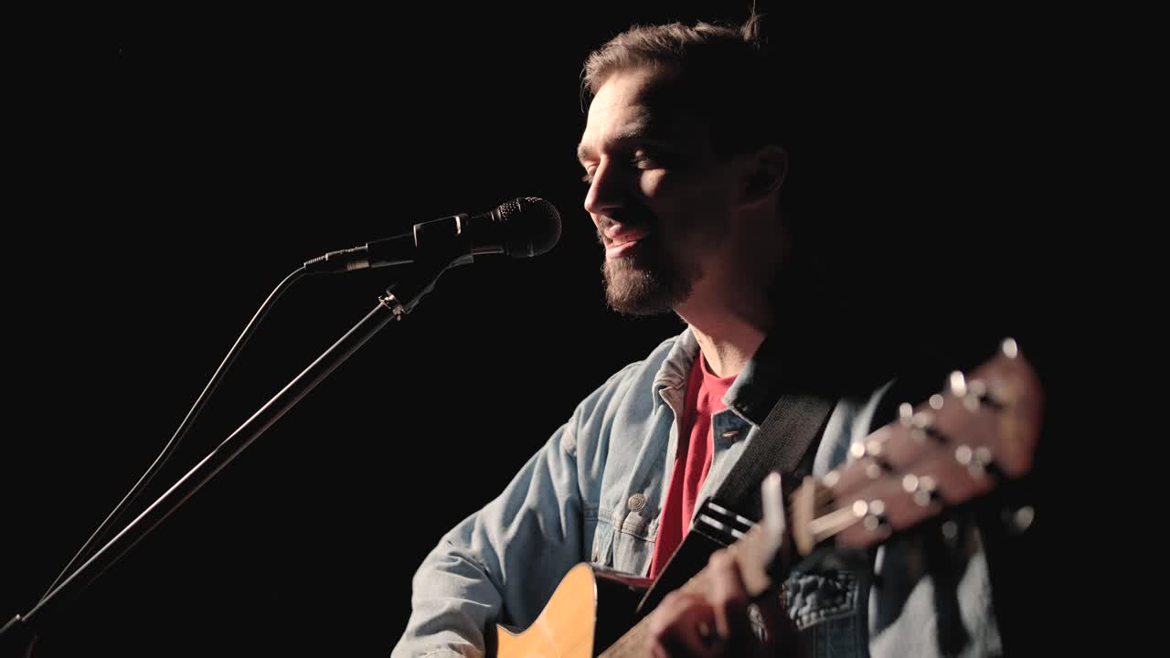 un músico está tocando la guitarra en un gran escenario con miembros de la audiencia sosteniendo linternas en el fondo. el auditorio está lleno de hermosas luces parpadeantes.