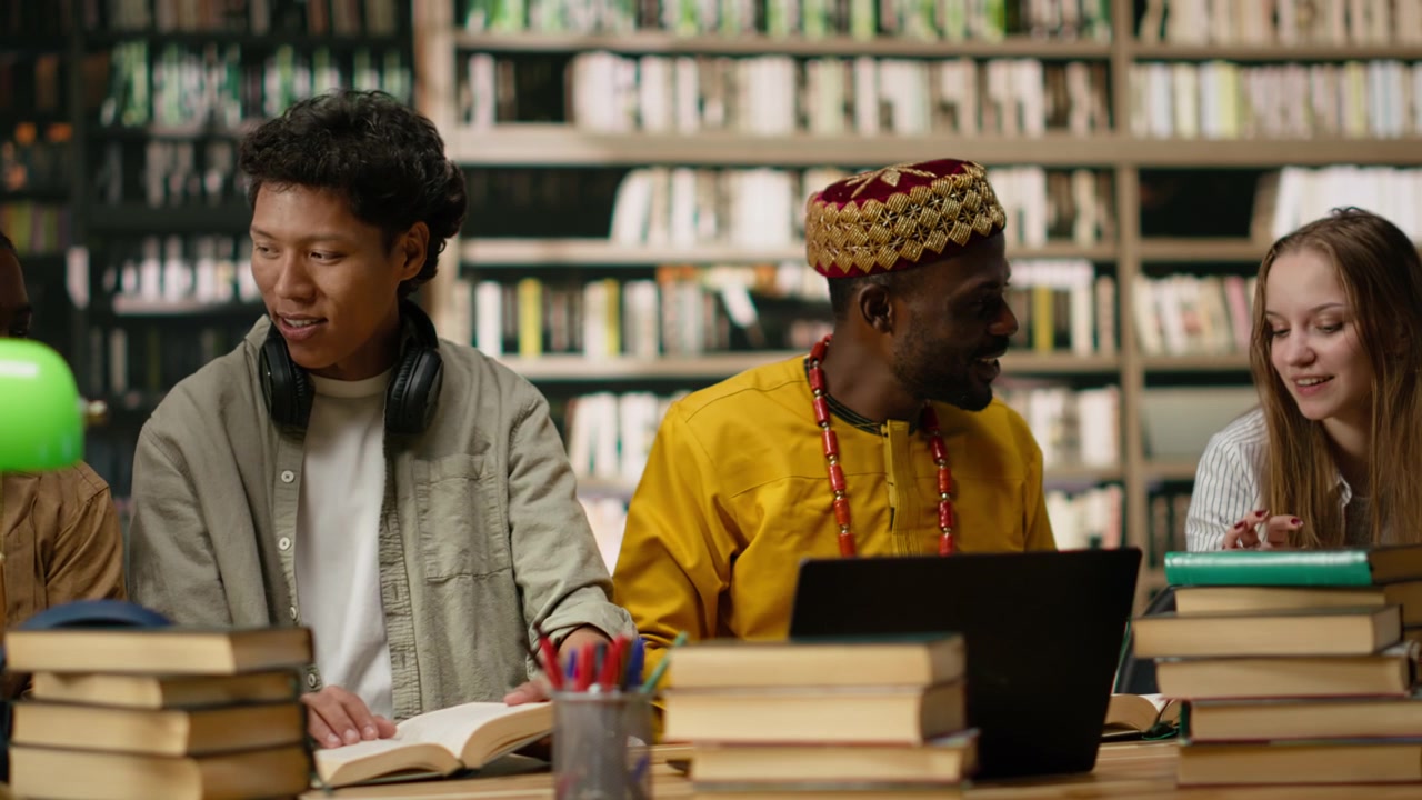 Studenti diversi discutono i compiti durante uno studio di gruppo attorno a un tavolo della biblioteca.