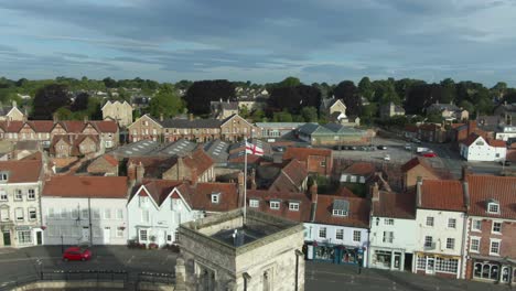 drone parallax around english village market town church with st georges flag flying in the wind on cloudy morning