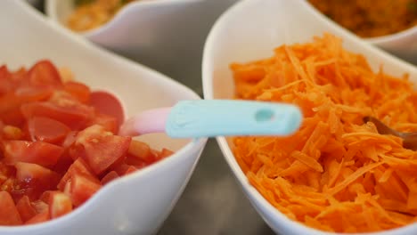 close-up of bowls with grated carrots and diced tomatoes at a salad bar