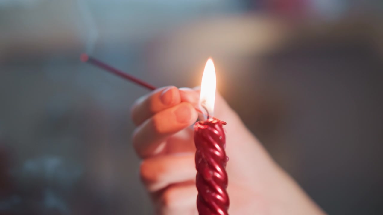 Mano che accende una candela rossa a spirale, primo piano di dita affusolate che accendono un fiammifero, fiamma calda e fumo, spirale di cera che si scioglie, tavolo da tarocchi sfocato sullo sfondo, concentrazione rituale silenziosa e preveggenza