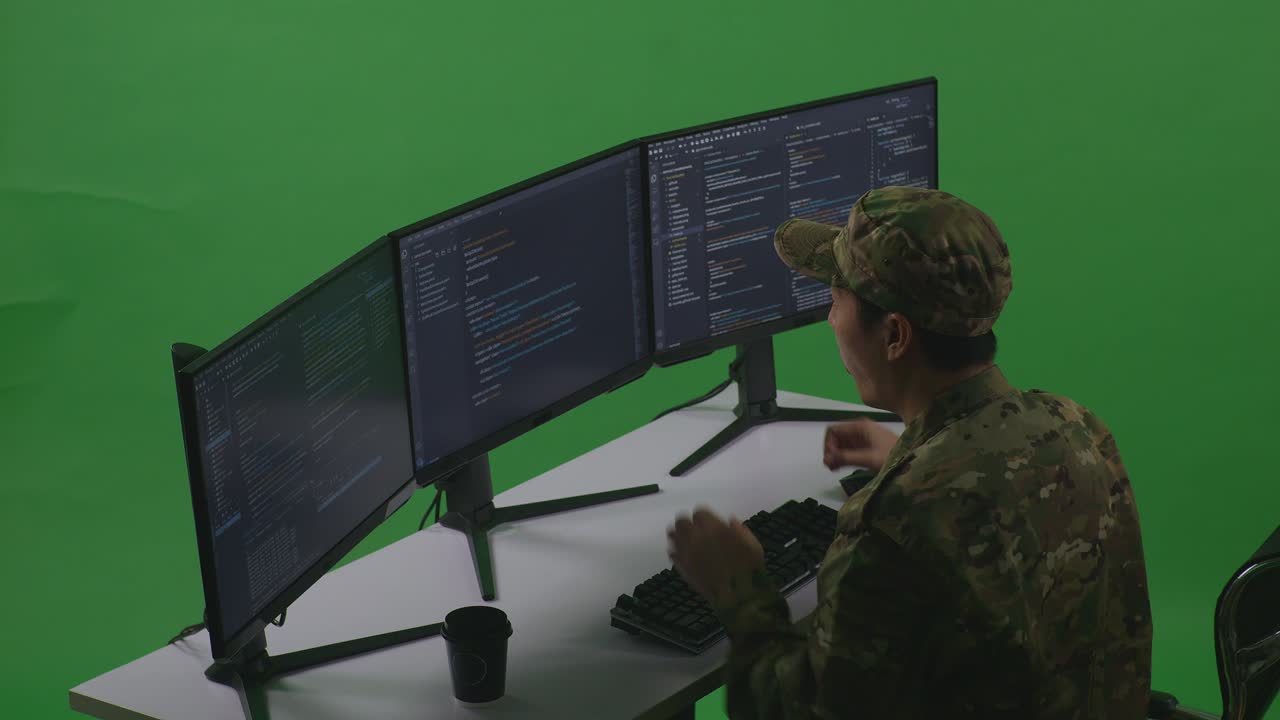 Side View Of Happy Asian Man Soldier Developer Celebrating While Write Code With Multiple Computer Screens In Green Screen Studio