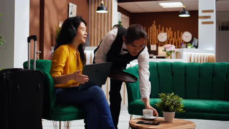 Asian-woman-on-laptop-ordering-coffee-in-lounge-area