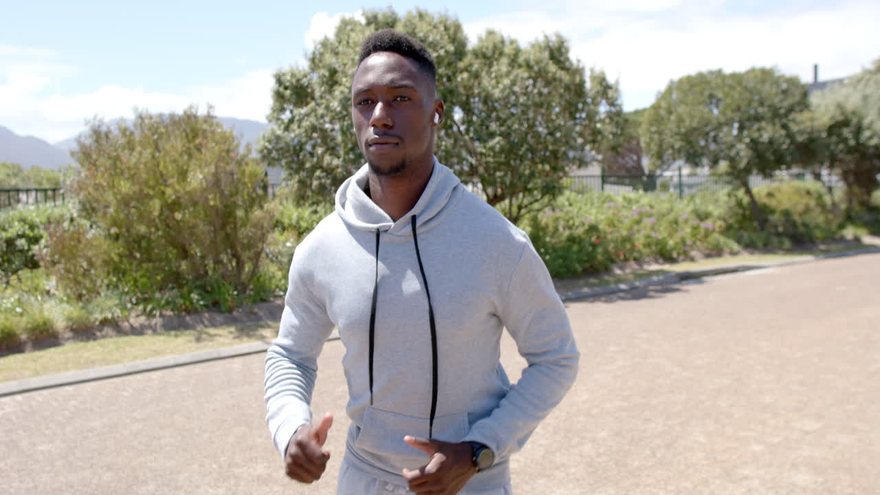 Focused african american man jogging with headphones on street on sunny day, slow motion