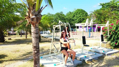 two girls exercising on the outdoor gym surrounded by beautiful flowers and tropical plants of vacations resort garden in thailand