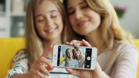 close up view of mother and cute girl taking a selfie with smartphone sitting on sofa in living room