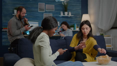 mixed race friends sitting on sofa holdings mobile in hands browsing on internet