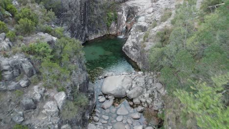 aerial pullback over emerald natural pool from waterfall, gerês national park, portugal