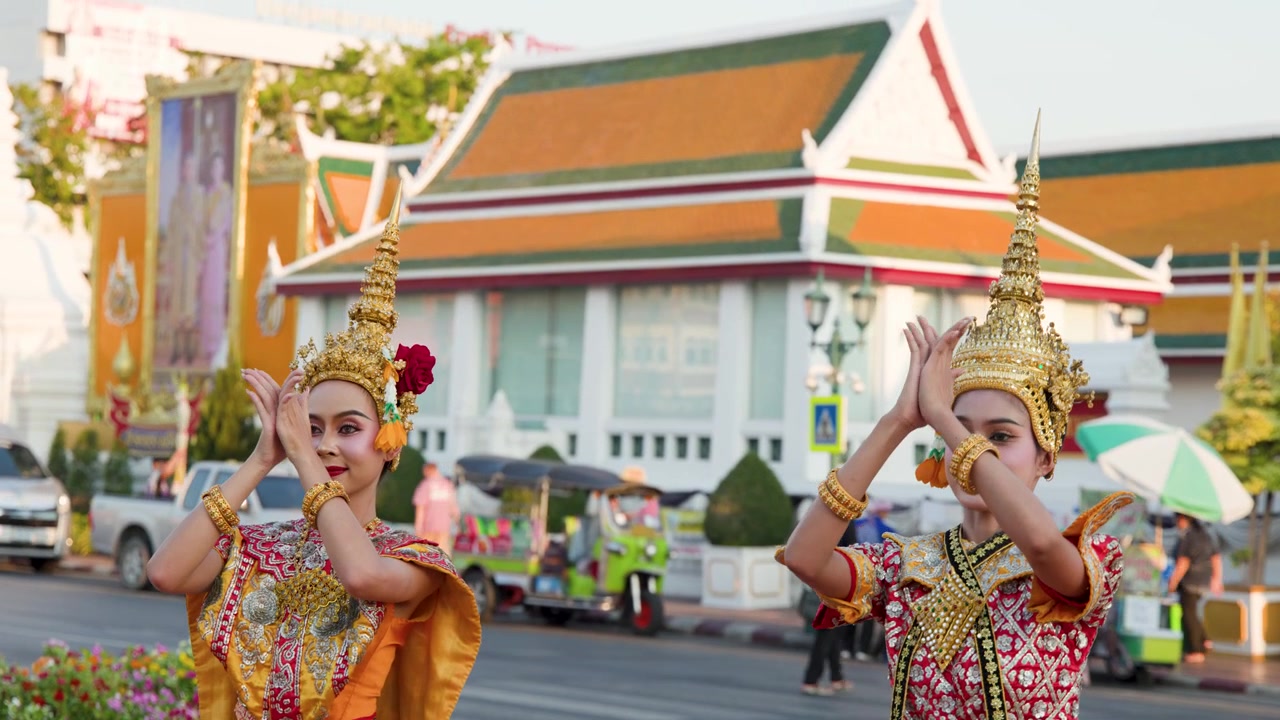 Due danzatrici thailandesi in sontuosi costumi tradizionali eseguono graziosi movimenti delle mani all'esterno di un tempio storico