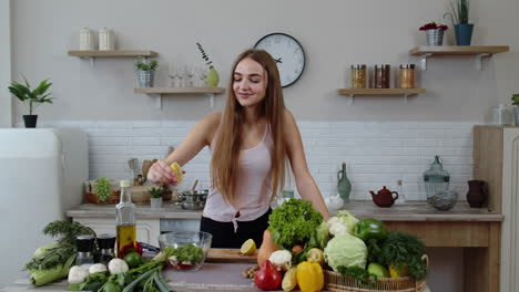 vegan girl in kitchen adding lemon juice to salad with raw vegetables. weight loss and diet concept