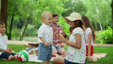 parents resting on blanket in park with children. kids blowing soap bubbles