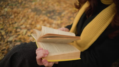 close-up of hands flipping through book pages thoughtfully, autumn leaves cover the ground as the person reads in a peaceful outdoor setting, immersed in the moment with curiosity and reflection