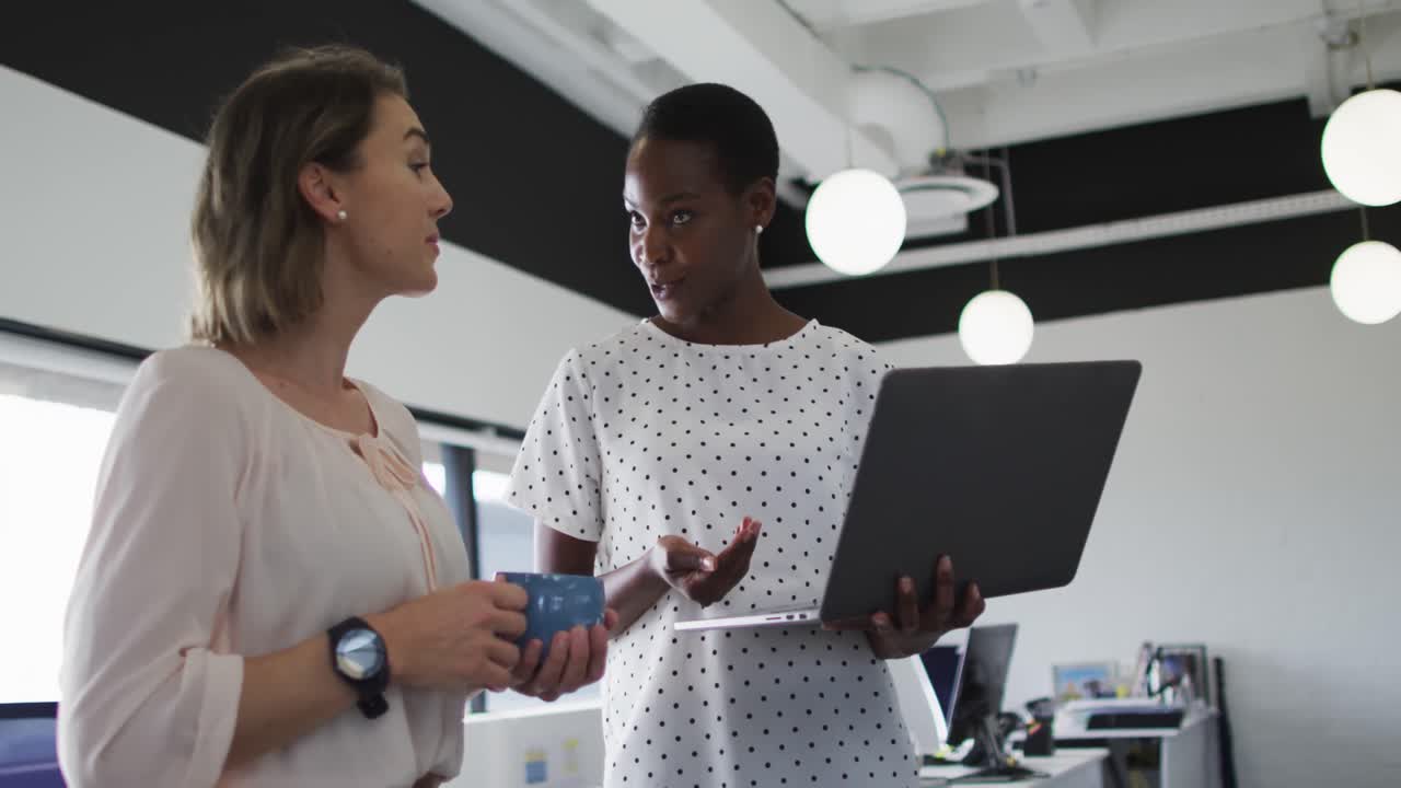 Two diverse female colleagues looking at laptop and discussing in office