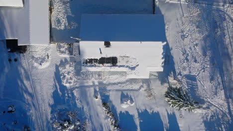 vista aérea por encima de un hombre limpiando la nieve de los paneles solares, en un techo de una casa independiente