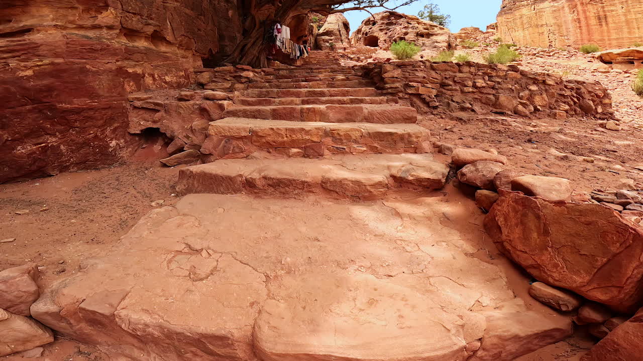 Stone stairs in the canyons. Some clothes hang on the rope tied to the dry tree. A walk by the stunning Petra, Jordan, West Asia.