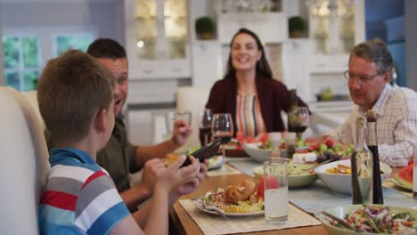 Glücklicher-Kaukasischer-Enkel,-Der-Während-Des-Familienessens-Ein-Selfie-Mit-Eltern-Und-Großvater-Am-Tisch-Macht