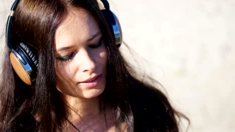 summer, against the background of the sea. beautiful woman, with long dark hair, listening to music on headphones from a mobile phone, device, outdoors, dances. enjoying music