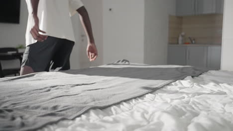 person in white shirt smoothing out grey blanket on bed, adjusting fabric to ensure smoothness, soft natural light brightening modern bedroom, minimalist interior, peaceful and organized environment