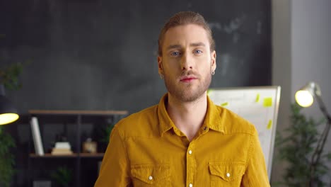 young handsome man in yellow shirt with crossed hands looking at camera with serious face in the office