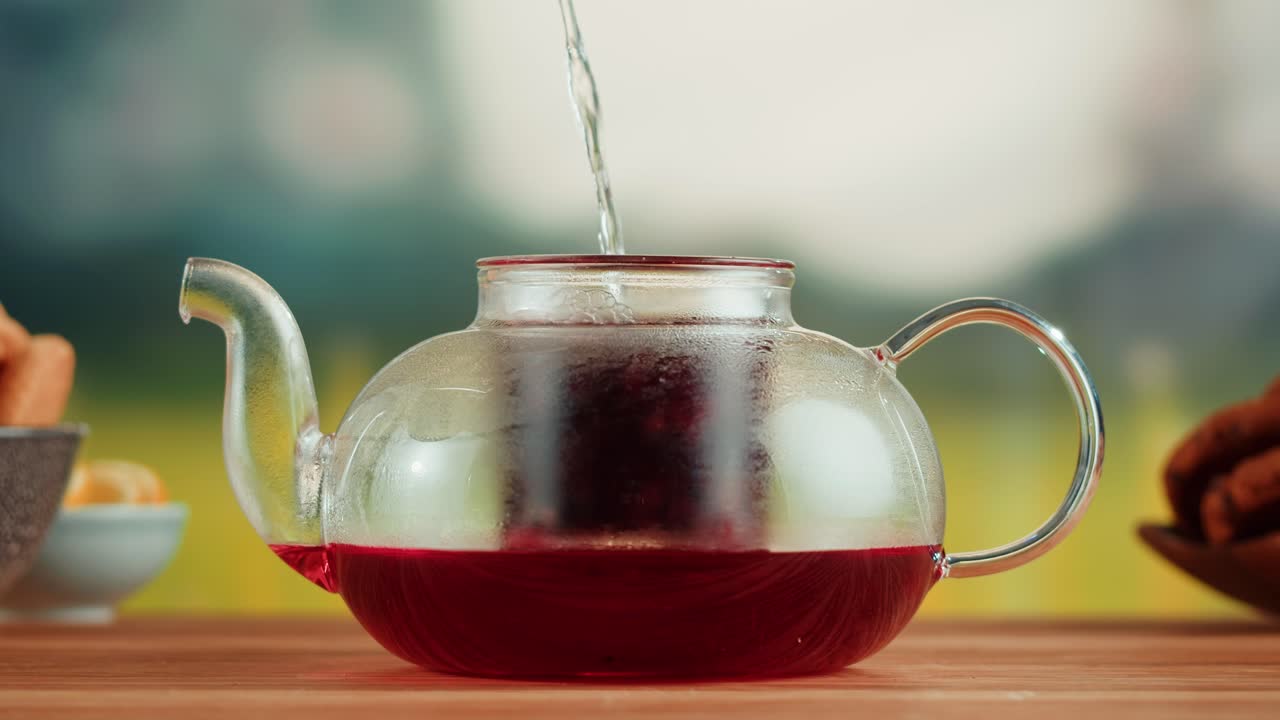Pouring hot water into a glass teapot to brew herbal tea